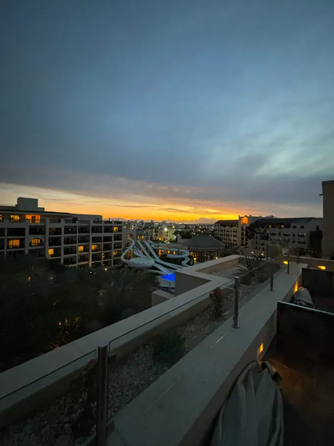 Abendrot über den Hotelgebäuden, darunter die Rutschen und ein beleuchtetes Becken, am Horizont eine Bergkette