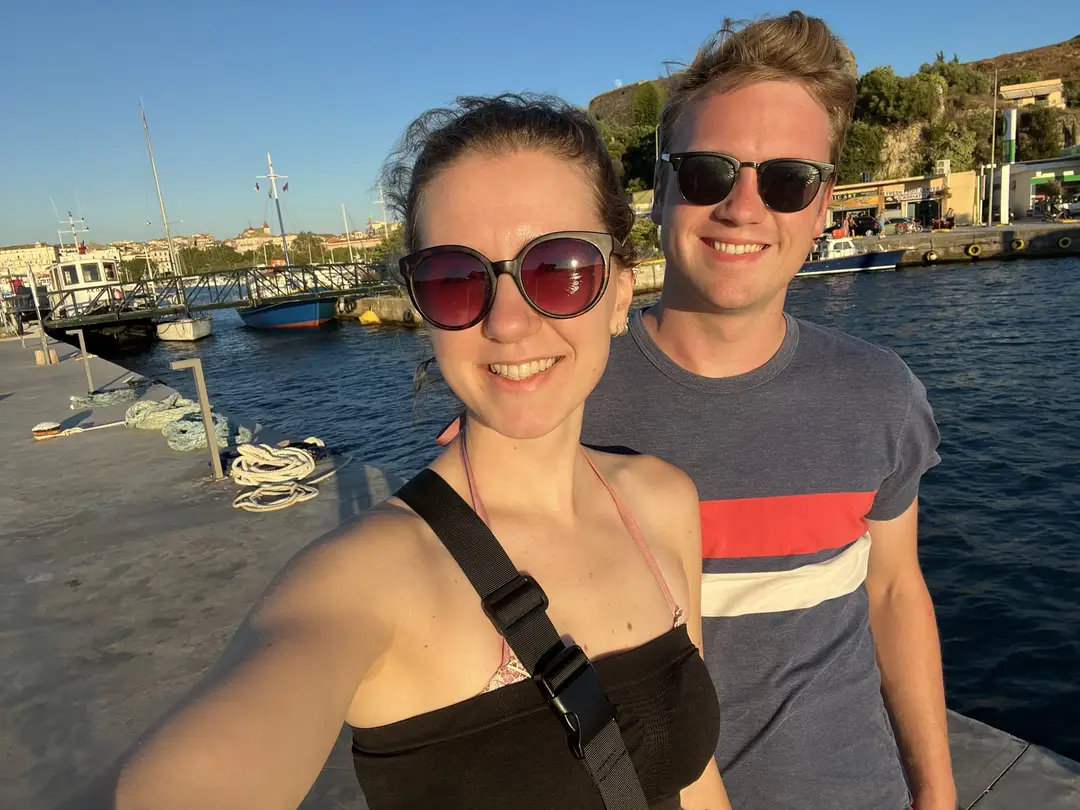 Selfie von Rebecca und Max in der Abendsonne auf einer Mole, hinter ihnen Boote im Hafen