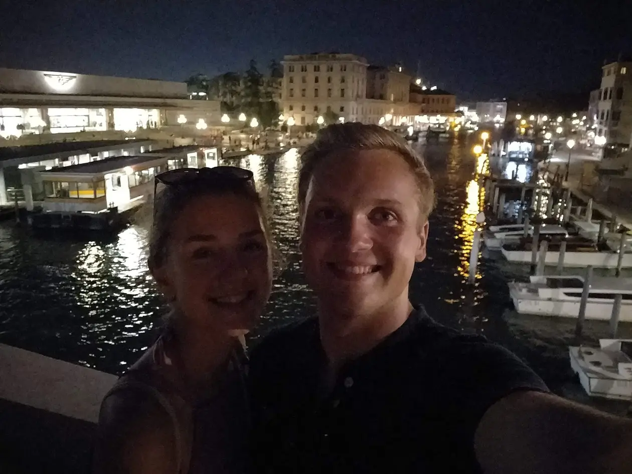 Selfie von Rebecca und Max bei Nacht, hinter ihnen beleuchtete Anleger und Boote am Canal Grande