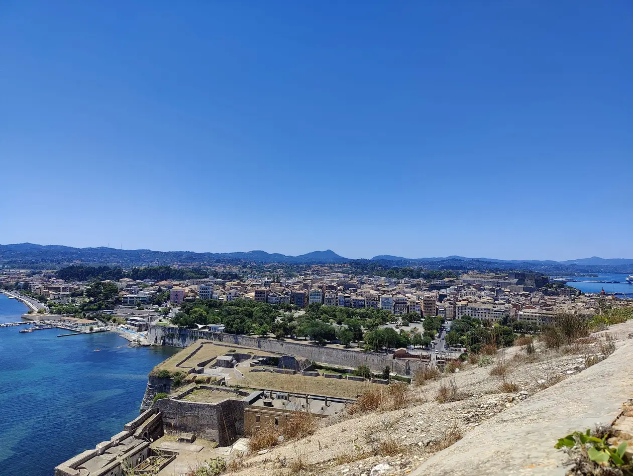 Blick von der Alten Festung über ihre Gebäude hinweg auf die Dächer der Altstadt, links das Meer, dahinter Hügel