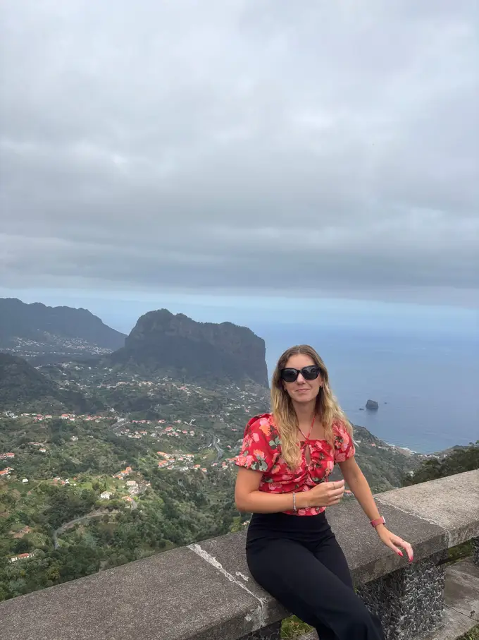 Person sitzt auf einer Mauer am Aussichtspunkt, dahinter die Aussicht auf die Nordküste