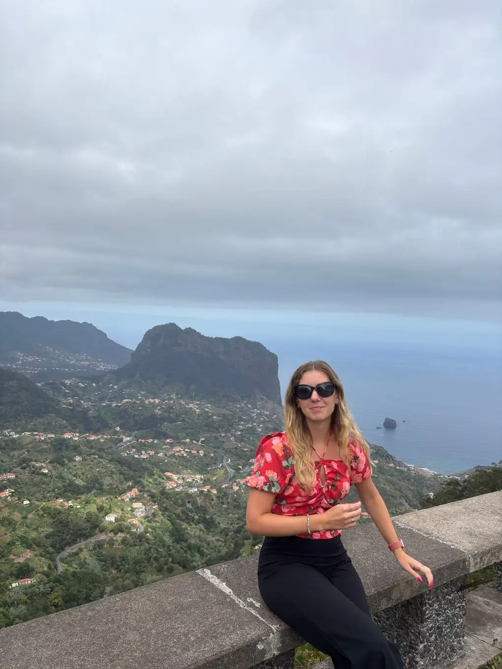 Person sitzt auf einer Mauer am Aussichtspunkt, dahinter die Aussicht auf die Nordküste