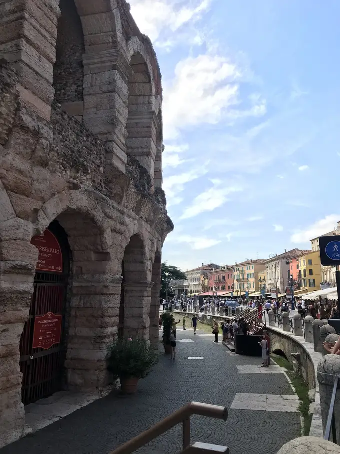Die hohen Steinbögen der Arena, daneben der breite Gehweg der Piazza Bra mit bunten Häusern