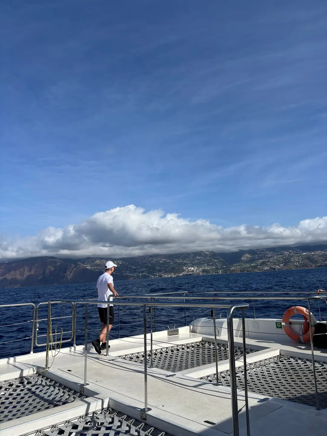 Mann steht an der Reling eines Bootsdecks, im Hintergrund die Steilküste unter Wolken