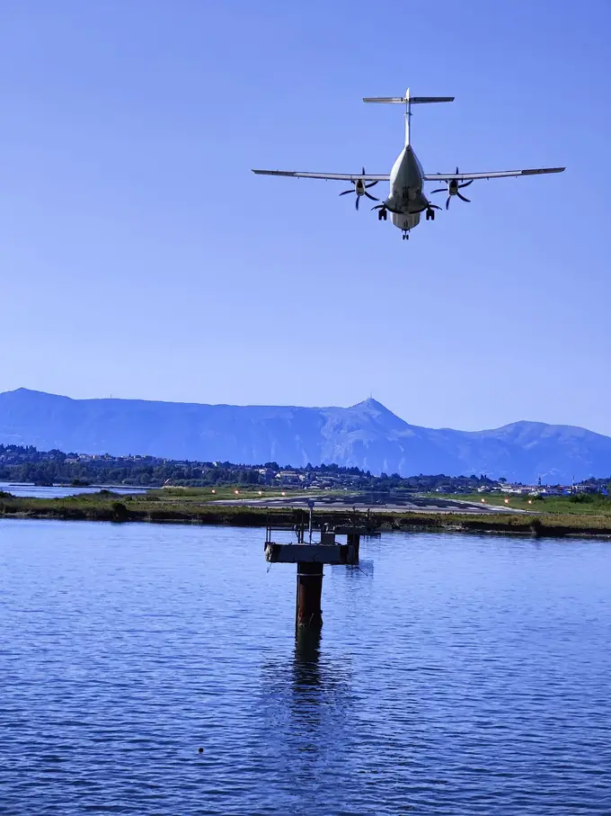 Eine Propellermaschine im Anflug über der Lagune, dahinter die Landebahn und Berge