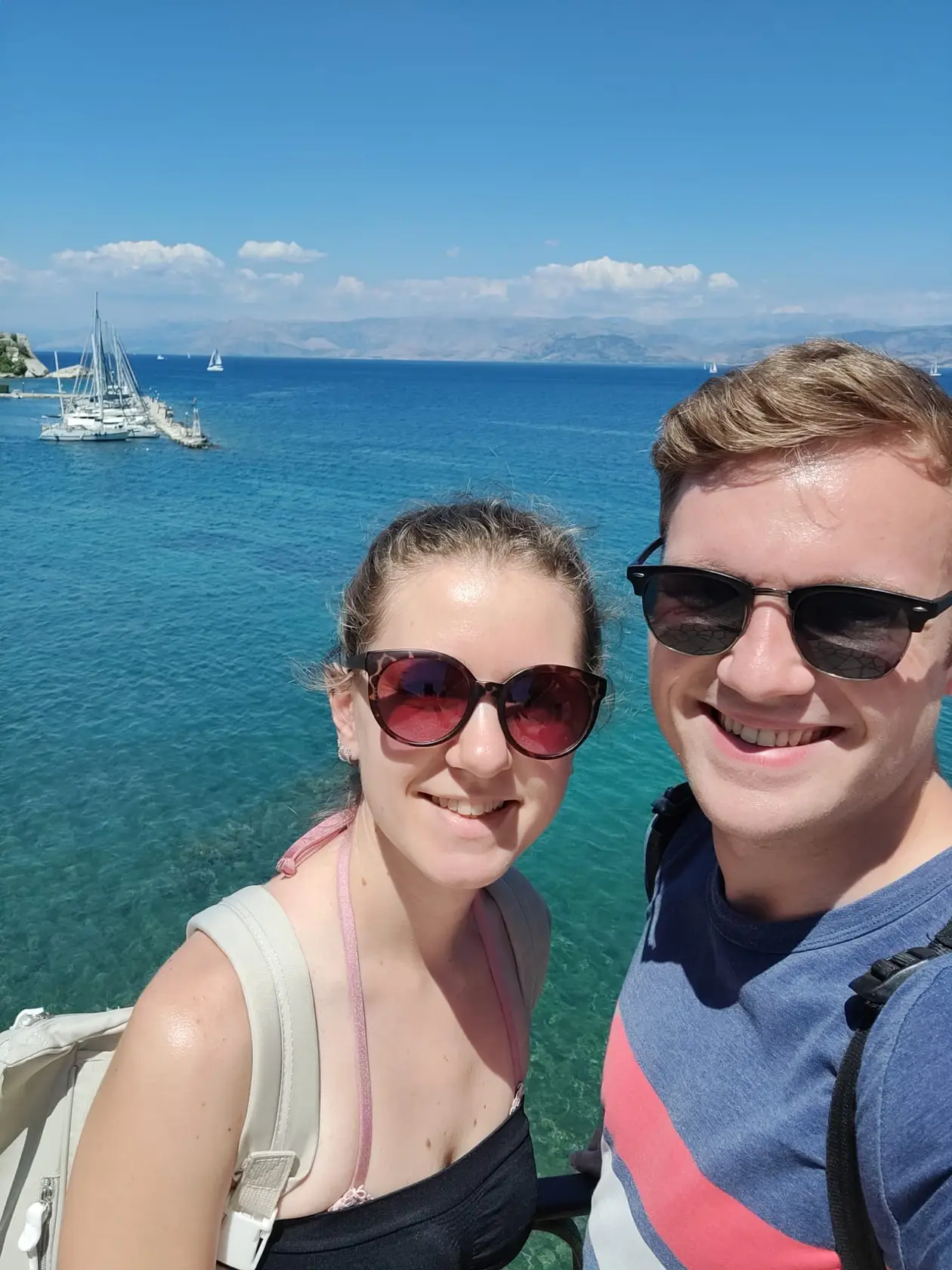 Selfie von Rebecca und Max mit Sonnenbrillen, hinter ihnen türkises Wasser, Segelboote und das Festland am Horizont