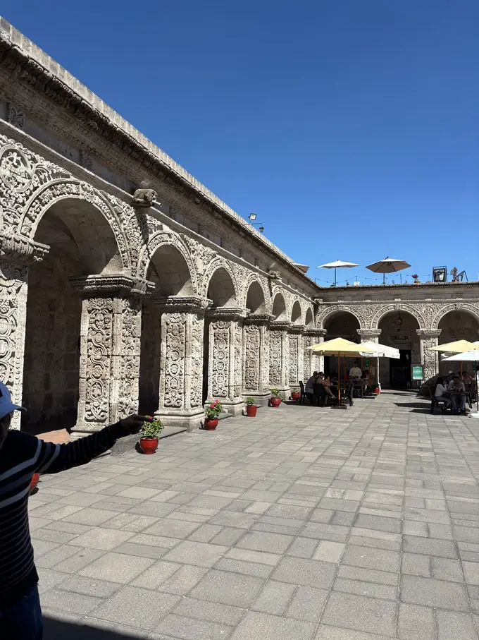 Innenhof mit steinernen Arkaden voller Reliefs, hinten weiße Sonnenschirme