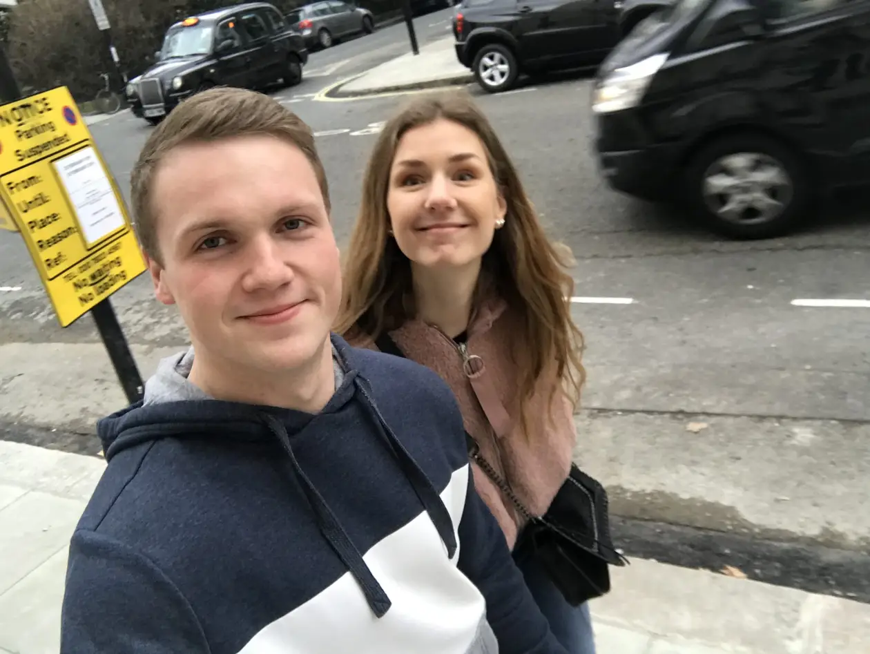 Selfie von Max und Rebecca an einer Straßenecke, dahinter ein schwarzes Londoner Taxi und ein gelbes Halteverbotsschild