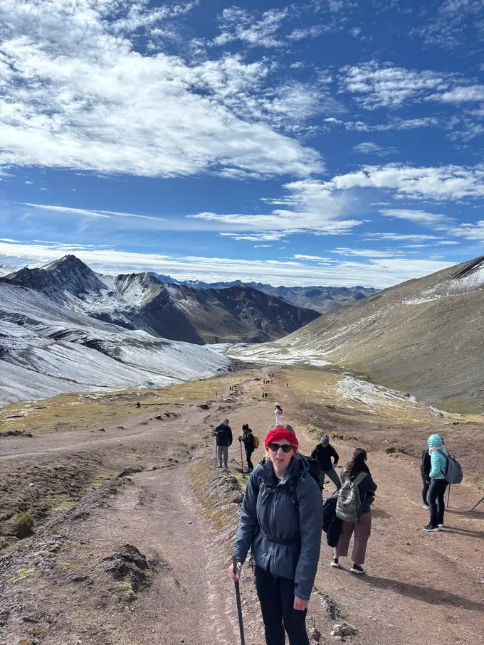 Rebecca mit Wanderstock auf dem Weg nach oben, um sie herum andere Wandernde, dahinter frisch verschneite Berge