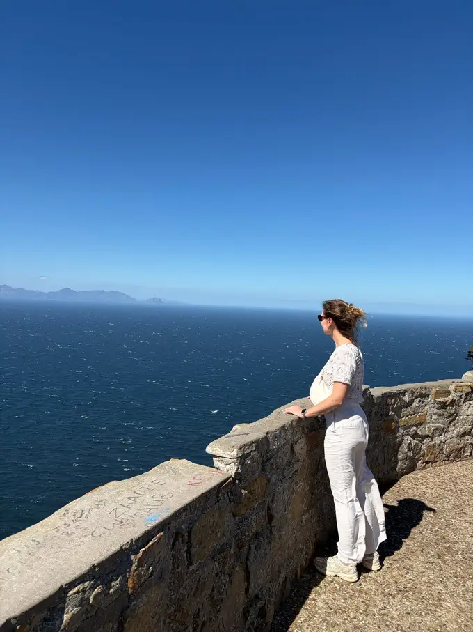 Rebecca mit vom Wind zerzausten Haaren an einer Aussichtsmauer mit Blick aufs Meer bei Cape Point