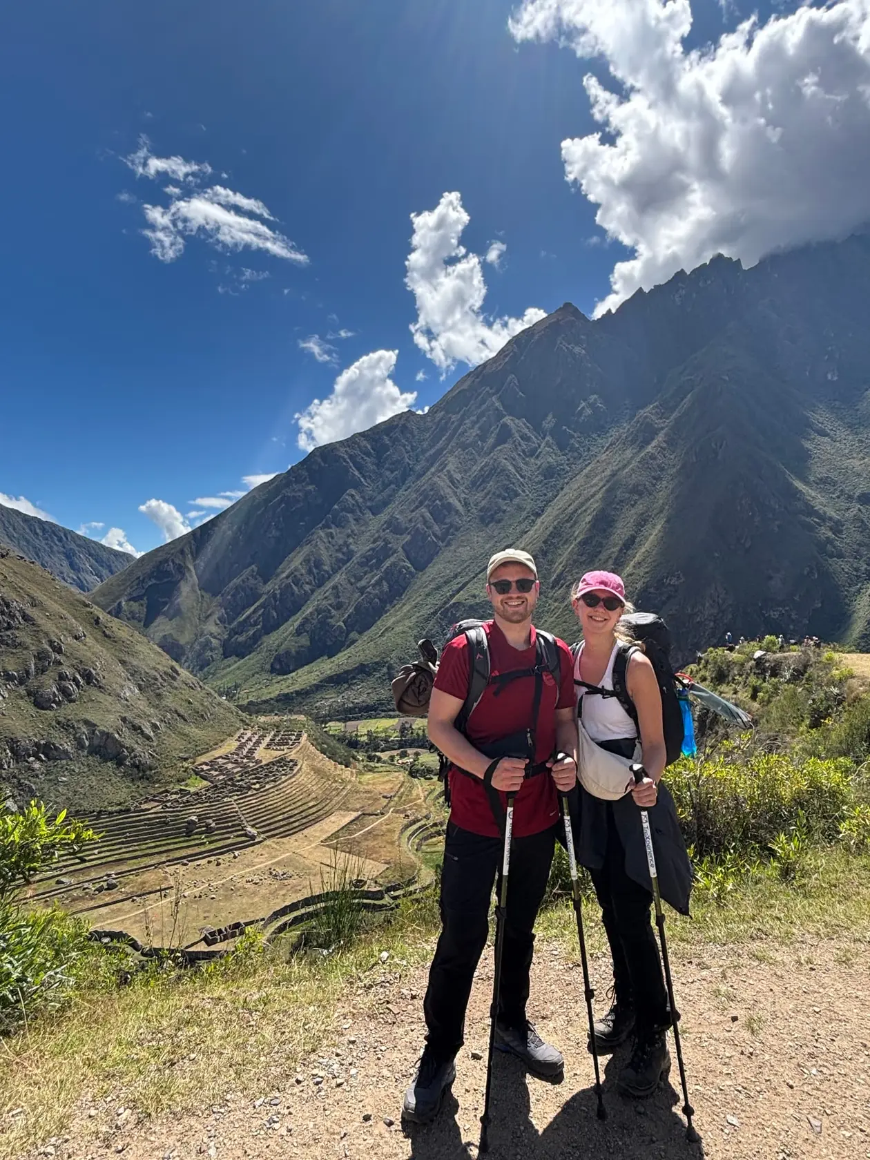 Max und Rebecca mit Wanderstöcken an einem Aussichtspunkt, hinter ihnen im Tal ausgedehnte Inka-Terrassen und ein hoher Bergrücken unter Wolken