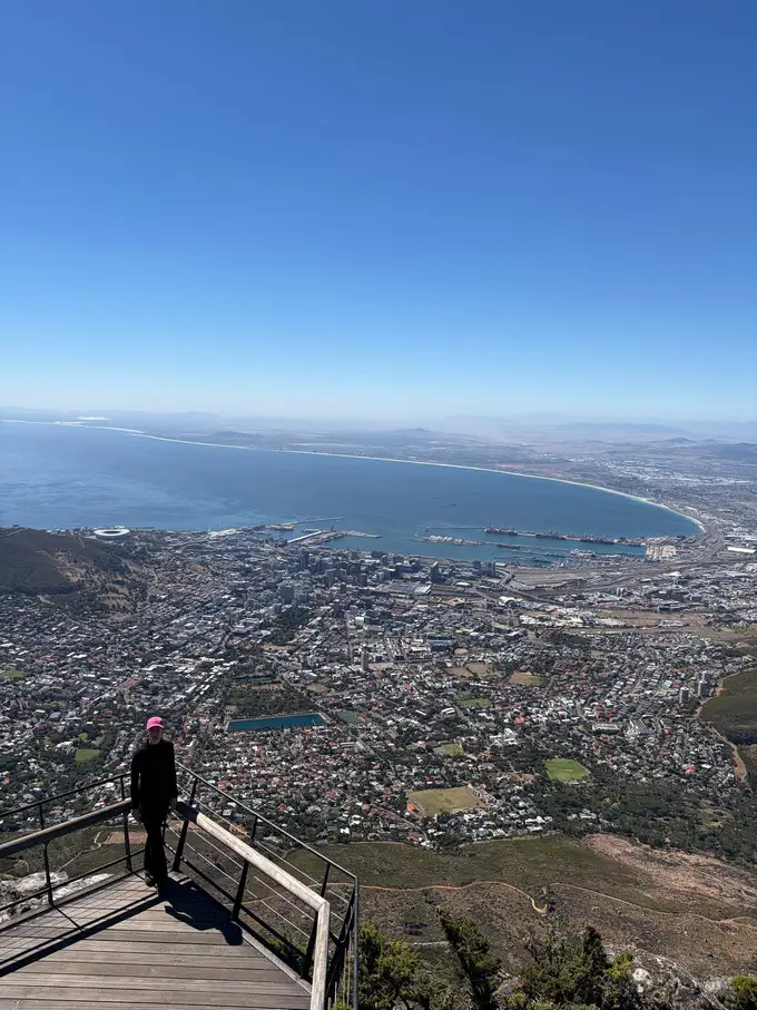 Eine Person steht an einem Aussichtsgeländer auf dem Tafelberg und blickt auf die Bucht von Kapstadt