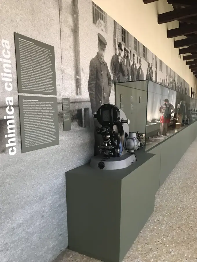 Langer Gang mit Holzdecke, an der Wand großformatige Schwarzweißfotos und Texttafeln, davor Vitrinen mit alten Geräten