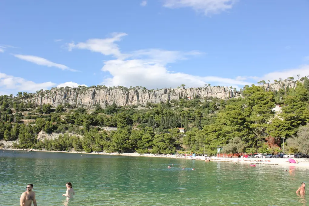 Eine Bucht unter einer hellen Kalkwand mit klarem Wasser und einigen Schwimmern