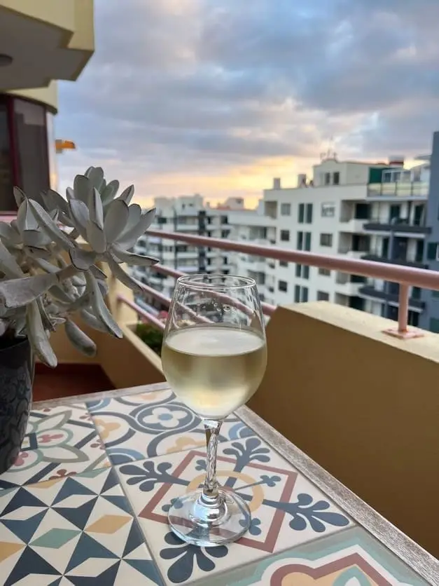 Weinglas auf einem gekachelten Balkontisch, davor eine Sukkulente, dahinter die Dächer von Funchal im Abendlicht