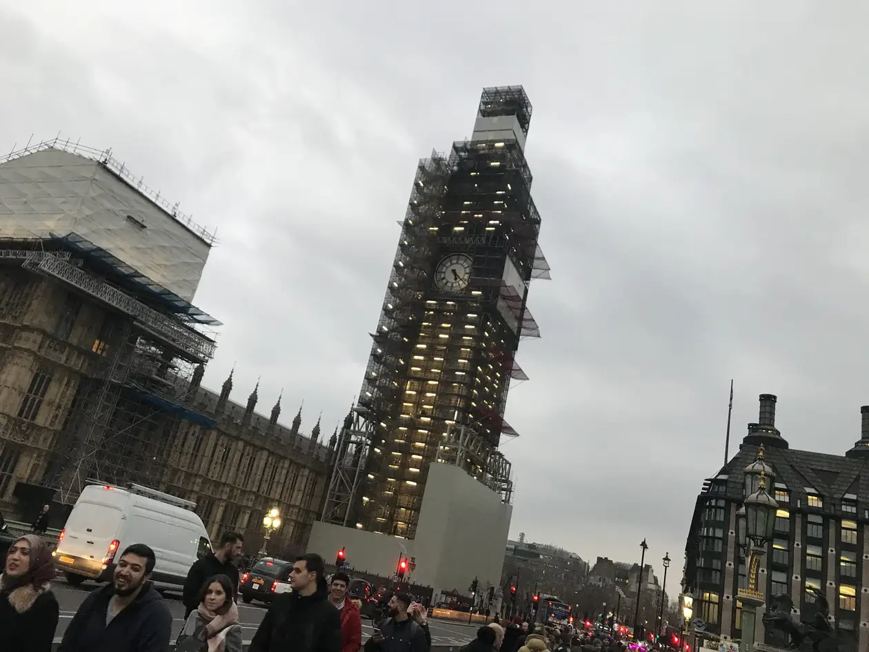 Der Elizabeth Tower mit Big Ben, fast vollständig eingerüstet, links das Parlamentsgebäude, unten Passanten und Verkehr in der Dämmerung