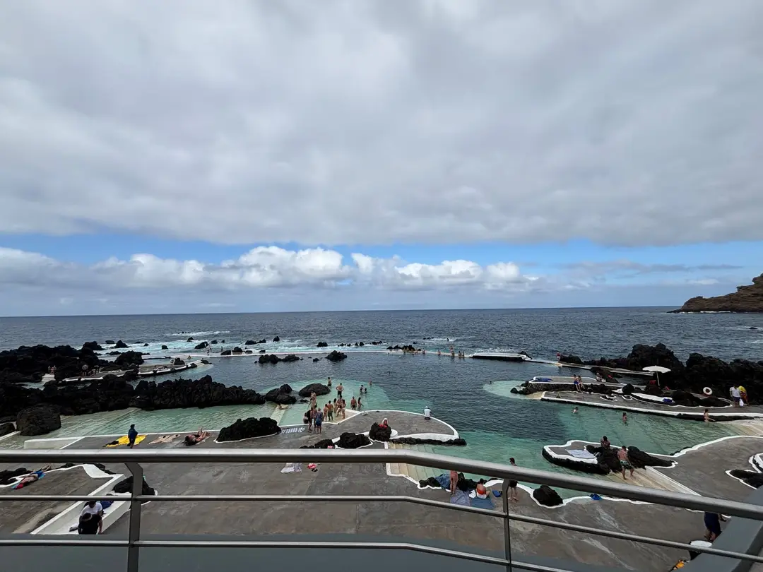 Blick von oben auf eine Anlage aus türkisfarbenen Lavabecken am Meer, mehrere Personen liegen und schwimmen dort