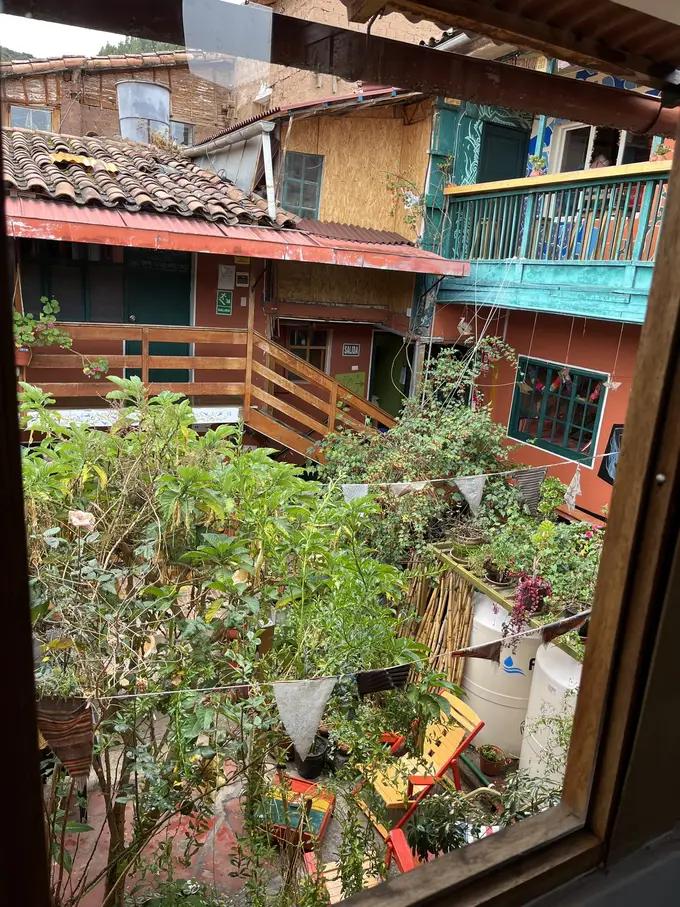 Blick aus dem Zimmerfenster in einen grünen Innenhof mit bunten Holzbalkonen und Wimpelketten