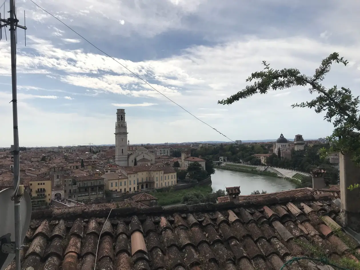 Blick über Ziegeldächer auf Verona mit einem hohen Glockenturm und der Etsch