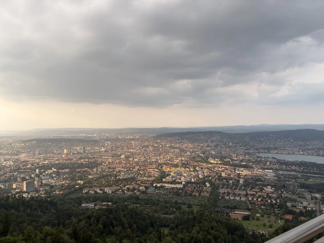 Blick von oben über das Häusermeer von Zürich bis zum See rechts, darüber dunkle Wolken mit einem hellen Streifen am Horizont
