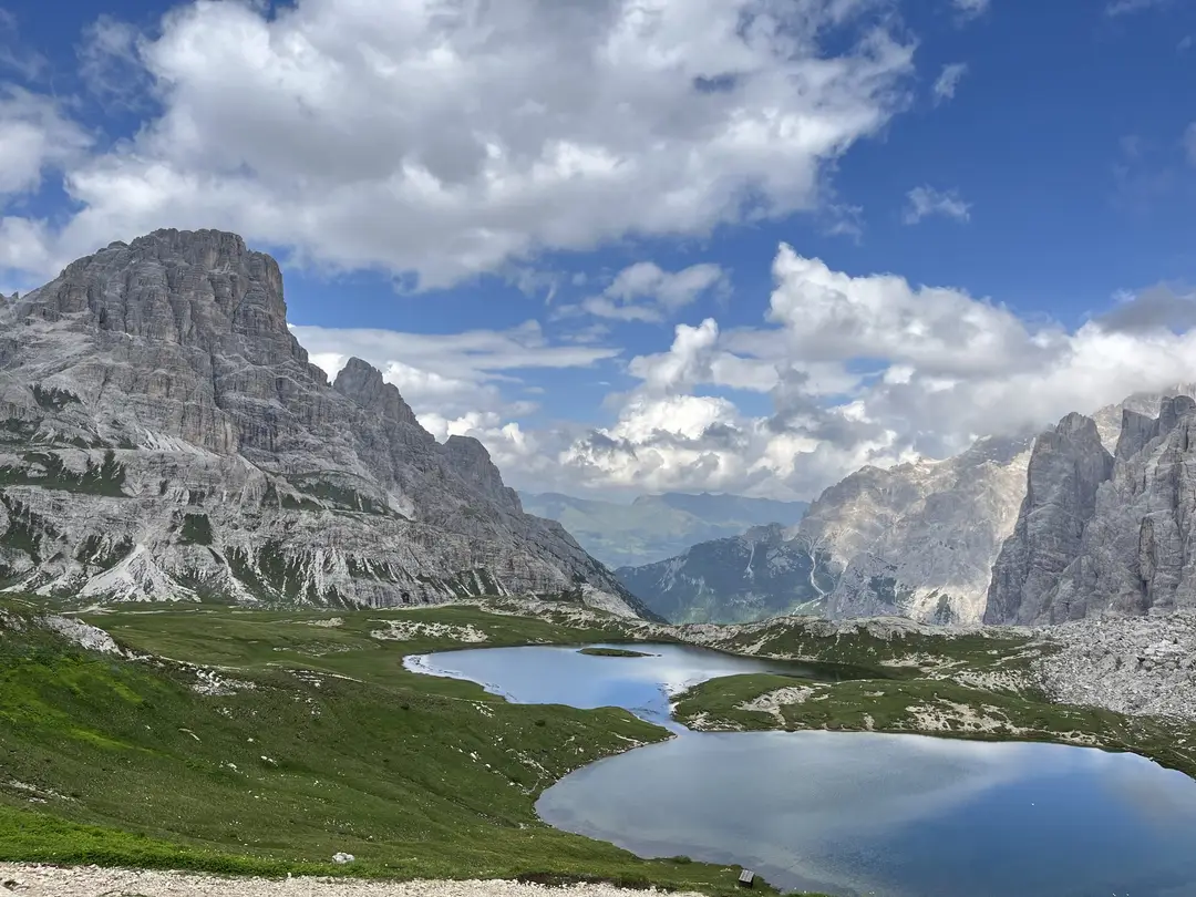 Zwei kleine Bergseen in grünen Almwiesen, links ein mächtiger grauer Felsberg, rechts steile Felswände, dazwischen der Blick in ein fernes Tal unter Wolken