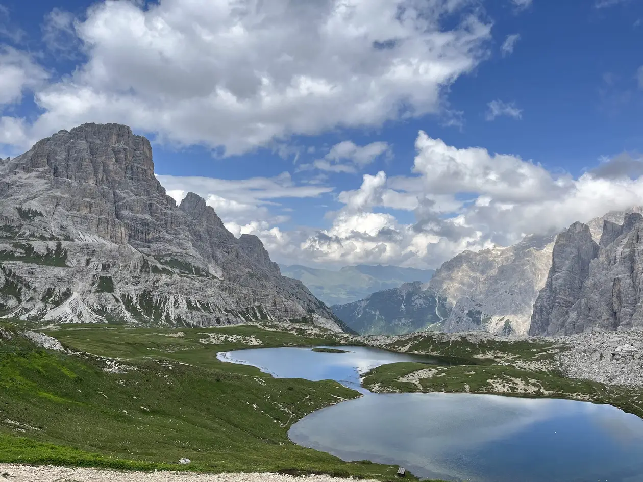 Zwei kleine Bergseen in grünen Almwiesen, links ein mächtiger grauer Felsberg, rechts steile Felswände, dazwischen der Blick in ein fernes Tal unter Wolken