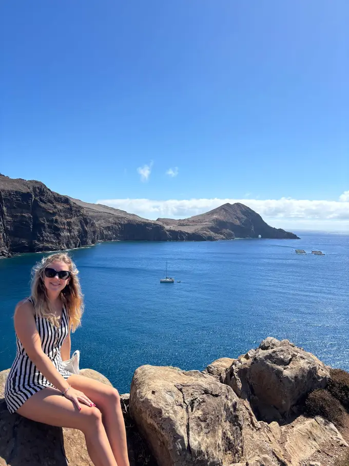 Rebecca sitzt auf einer Felskante, davor die schmale Halbinsel mit tiefblauem Wasser auf beiden Seiten