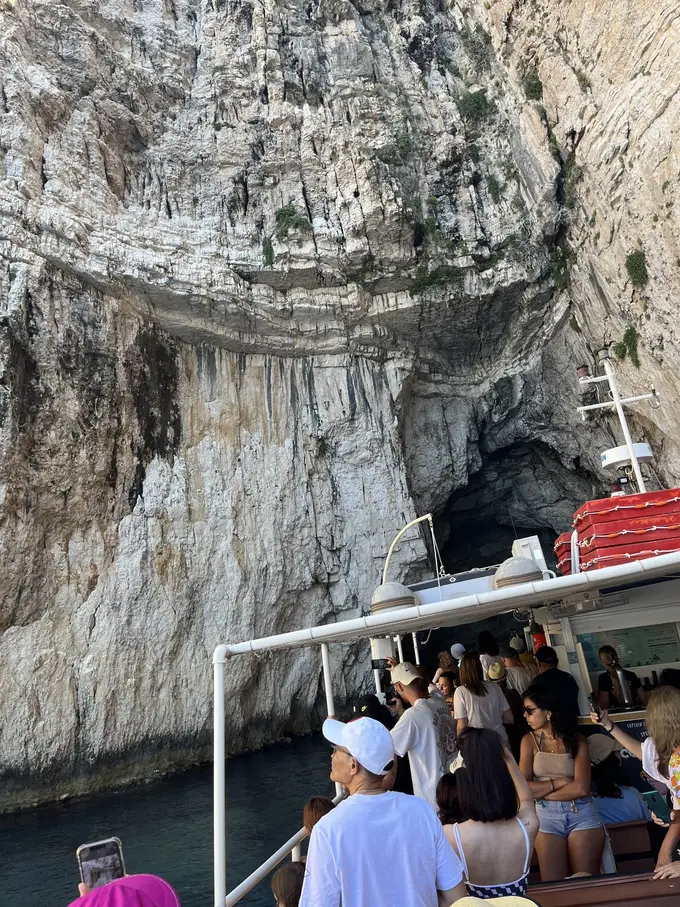 Ein voll besetztes Ausflugsboot fährt in eine Höhle unter einer hellen Felswand