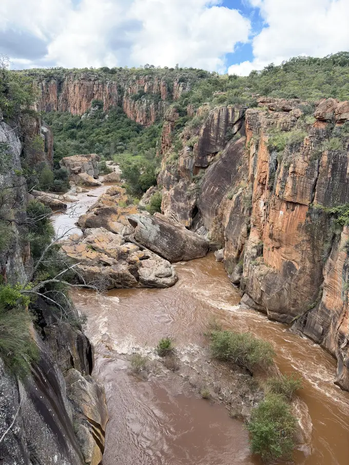 Schlucht mit rundgewaschenen Felslöchern, durch die sich lehmbraunes Flusswasser windet