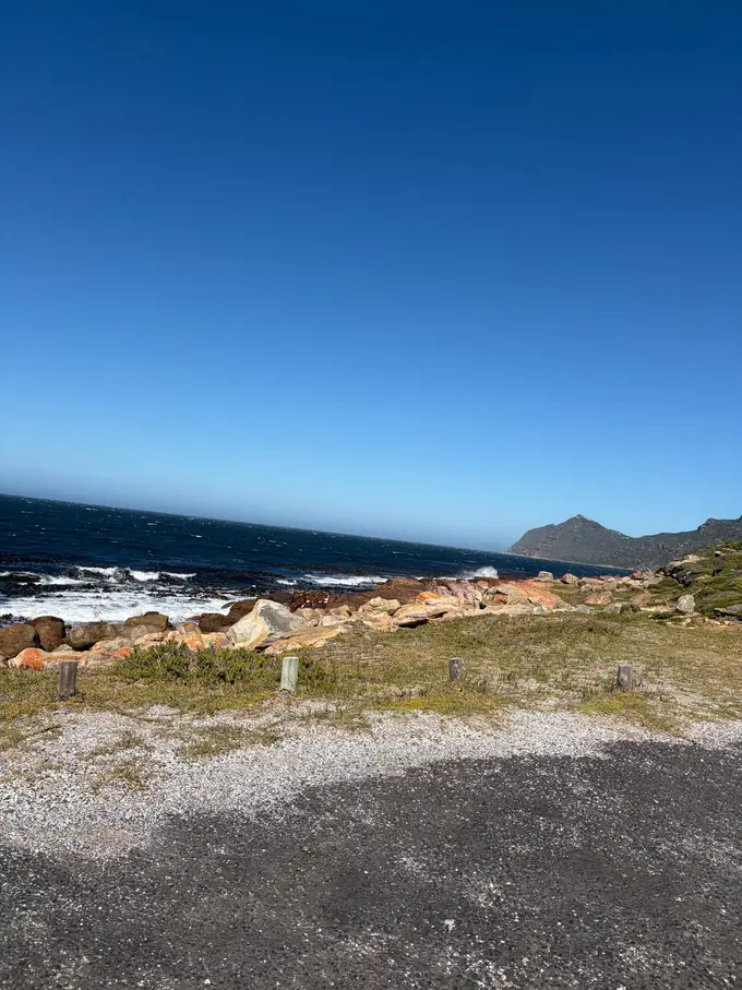 Felsige Küste der Buffels Bay mit brechenden Wellen, im Vordergrund ein Schotterparkplatz