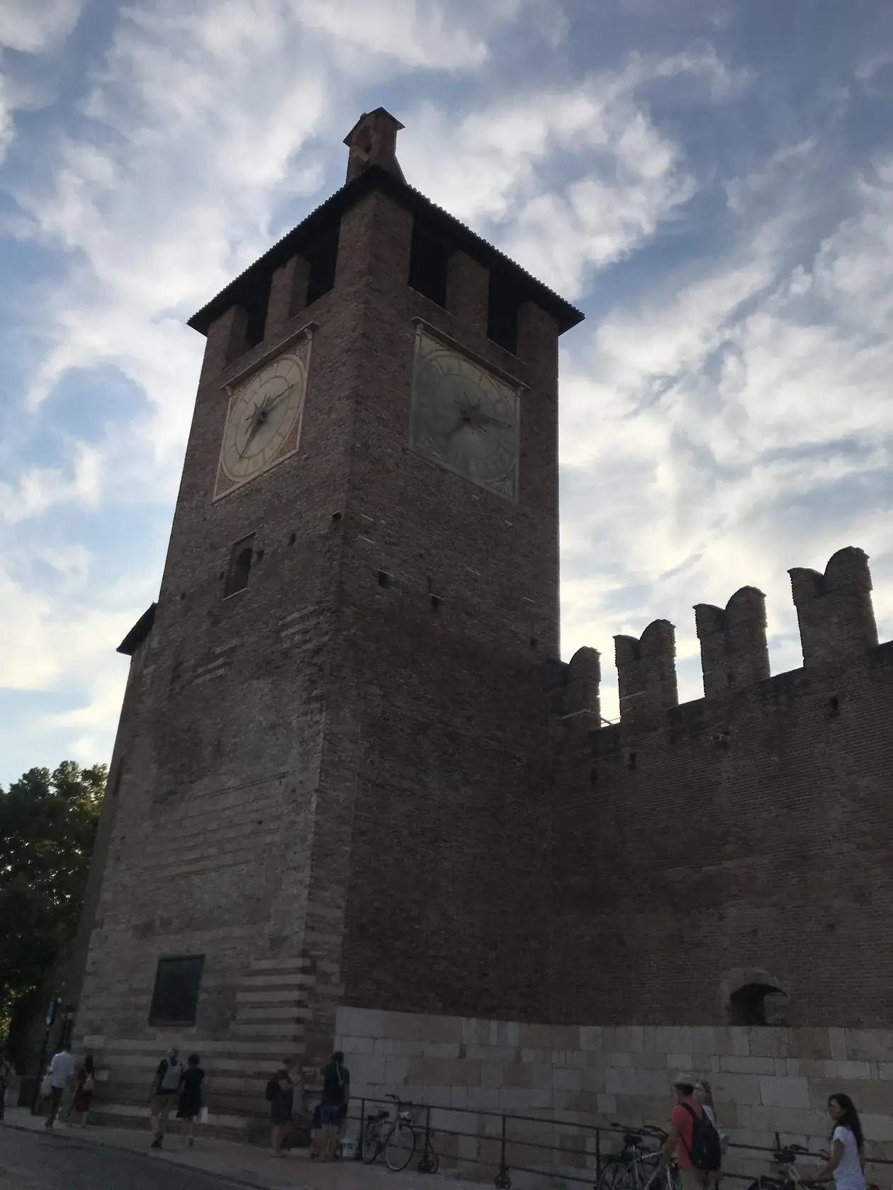 Der Backsteinturm des Castelvecchio mit Zinnenmauer vor einem Himmel mit Schleierwolken