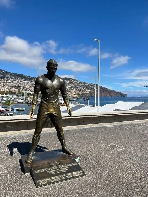 Goldene Ronaldo-Statue auf einem Sockel an der Marina von Funchal, dahinter der Hafen und bewaldete Hänge