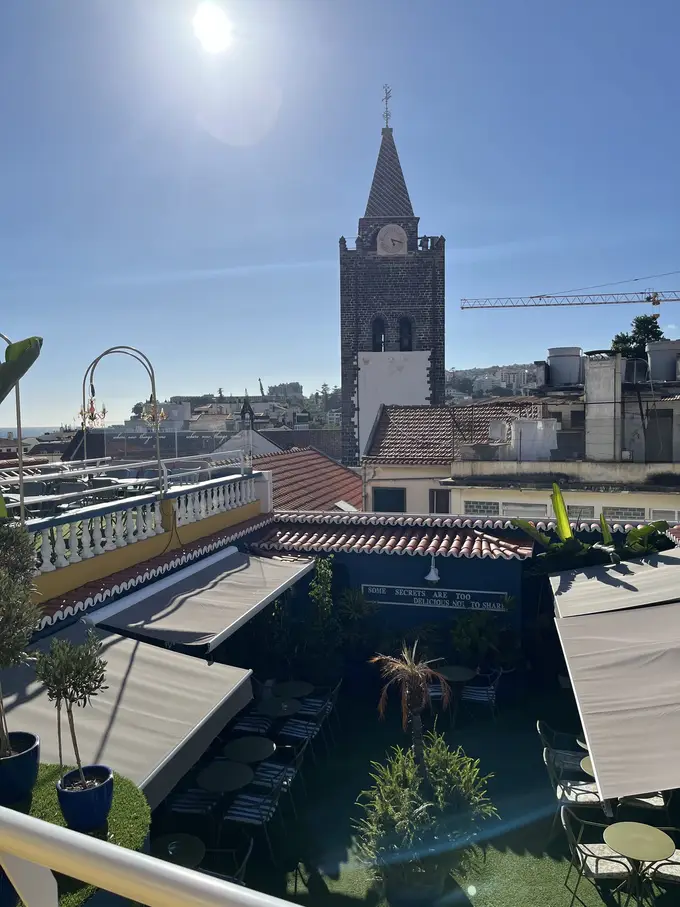 Dachterrasse mit Sonnenschirmen und Blick auf den Kirchturm von Funchal in der Sonne