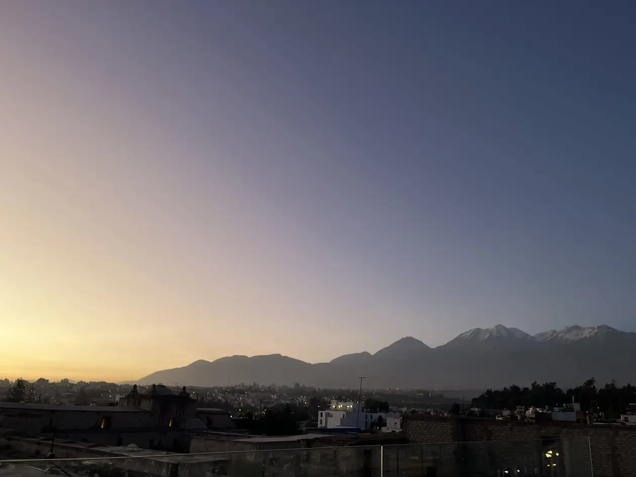 Blick von der Dachterrasse über die Stadt in der Dämmerung, am Horizont die Silhouette der Vulkane mit Schnee auf den Gipfeln