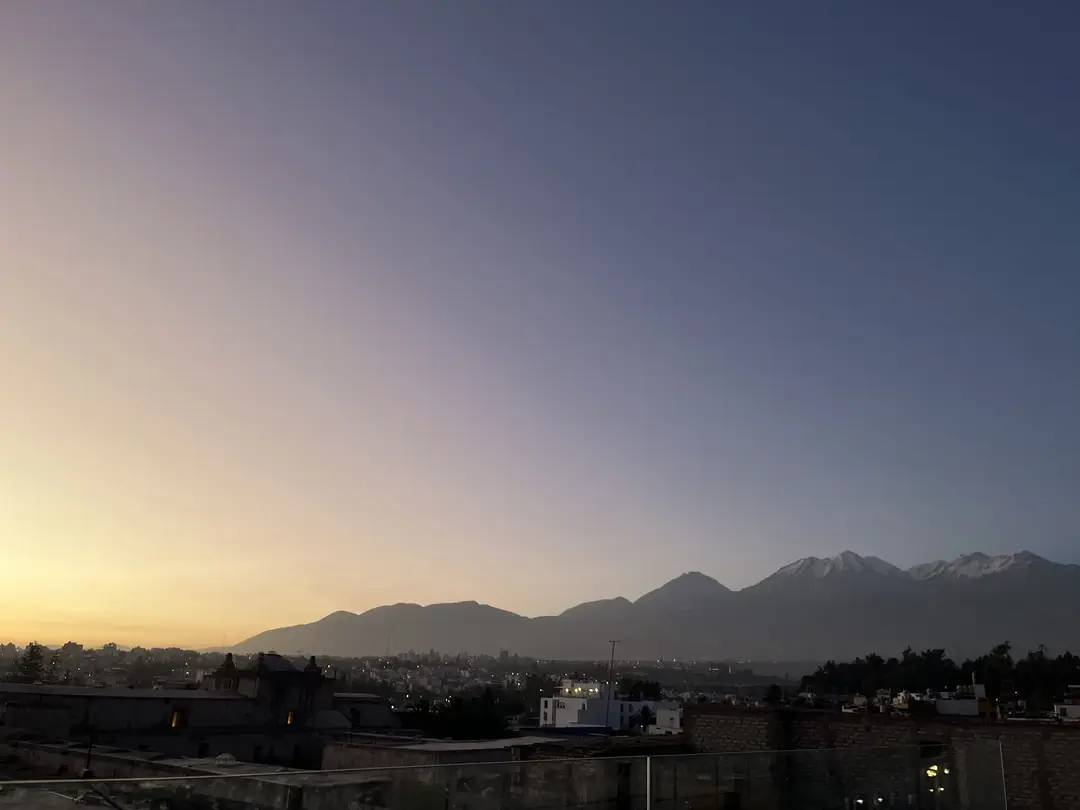 Blick von der Dachterrasse über die Stadt in der Dämmerung, am Horizont die Silhouette der Vulkane mit Schnee auf den Gipfeln