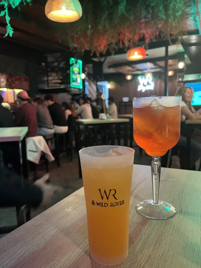 Zwei Drinks auf einem Tisch in der abendlichen Bar, auf dem Becher das Logo des Wild Rover