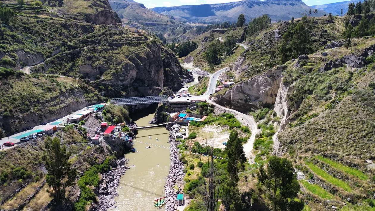 Drohnenblick auf ein enges Flusstal mit einer Brücke, bunten Dächern und grünen Terrassen an den Hängen