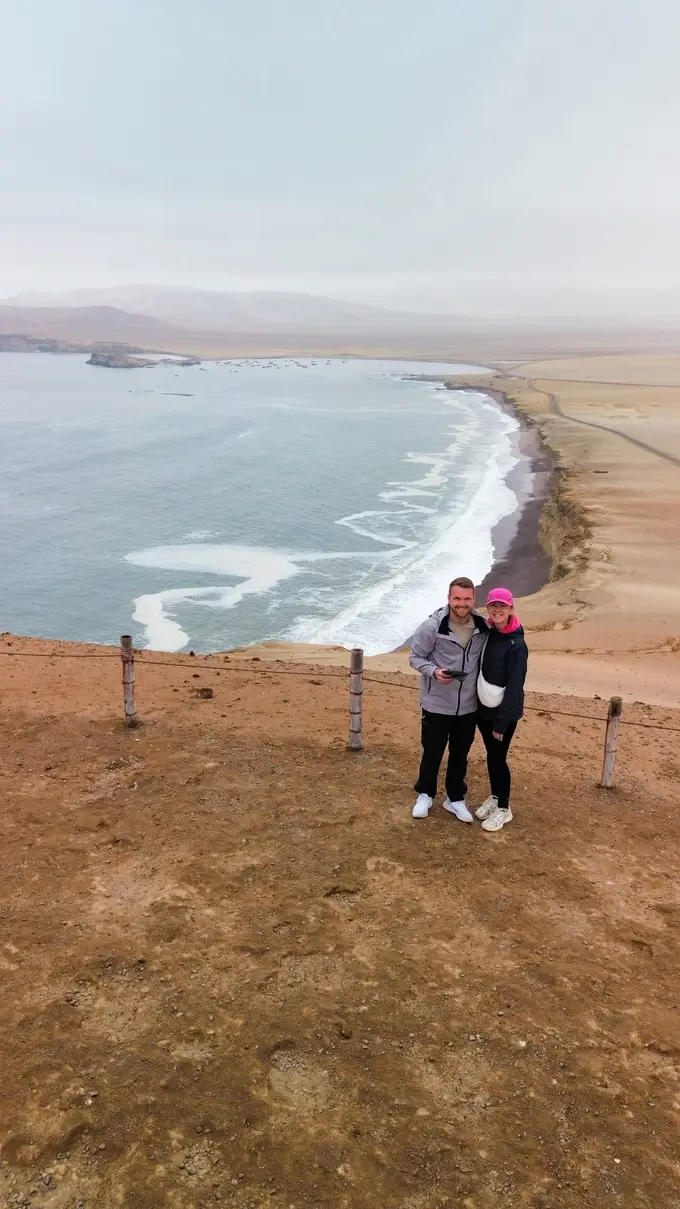 Drohnenbild von Max und Rebecca auf einer Anhöhe mit Absperrseil, dahinter eine lange Bucht mit weißer Brandung