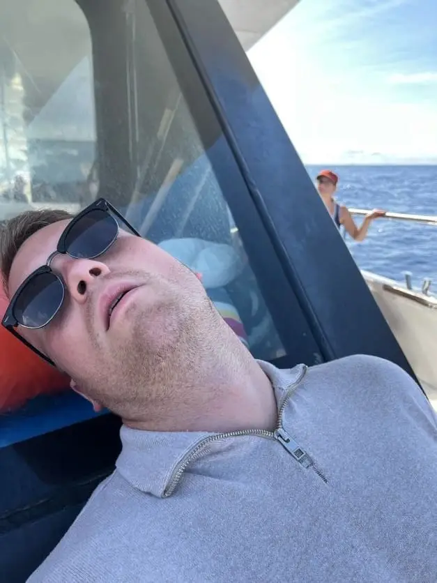 Mann mit Sonnenbrille lehnt mit geschlossenen Augen im Bootssitz zurück
