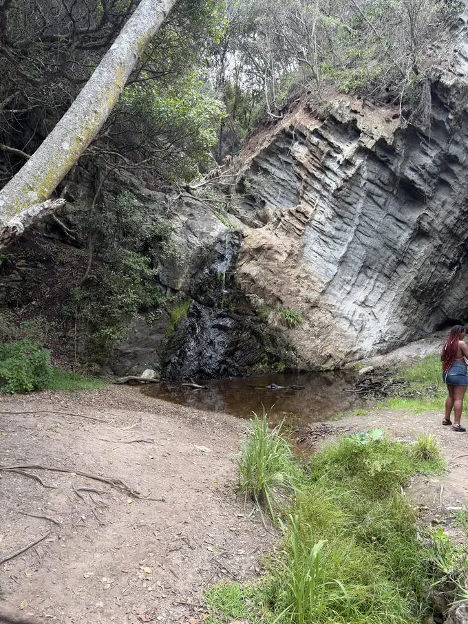 Geschichtete Felswand am Weg zur Mündung des Storms River, eine Person steht am Fuß des Felsens