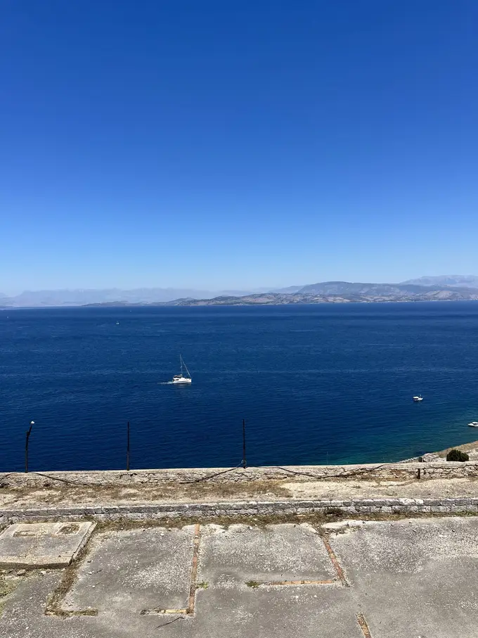 Von der Festungsmauer aus tiefblaues Meer, am Horizont die Berge des Festlands
