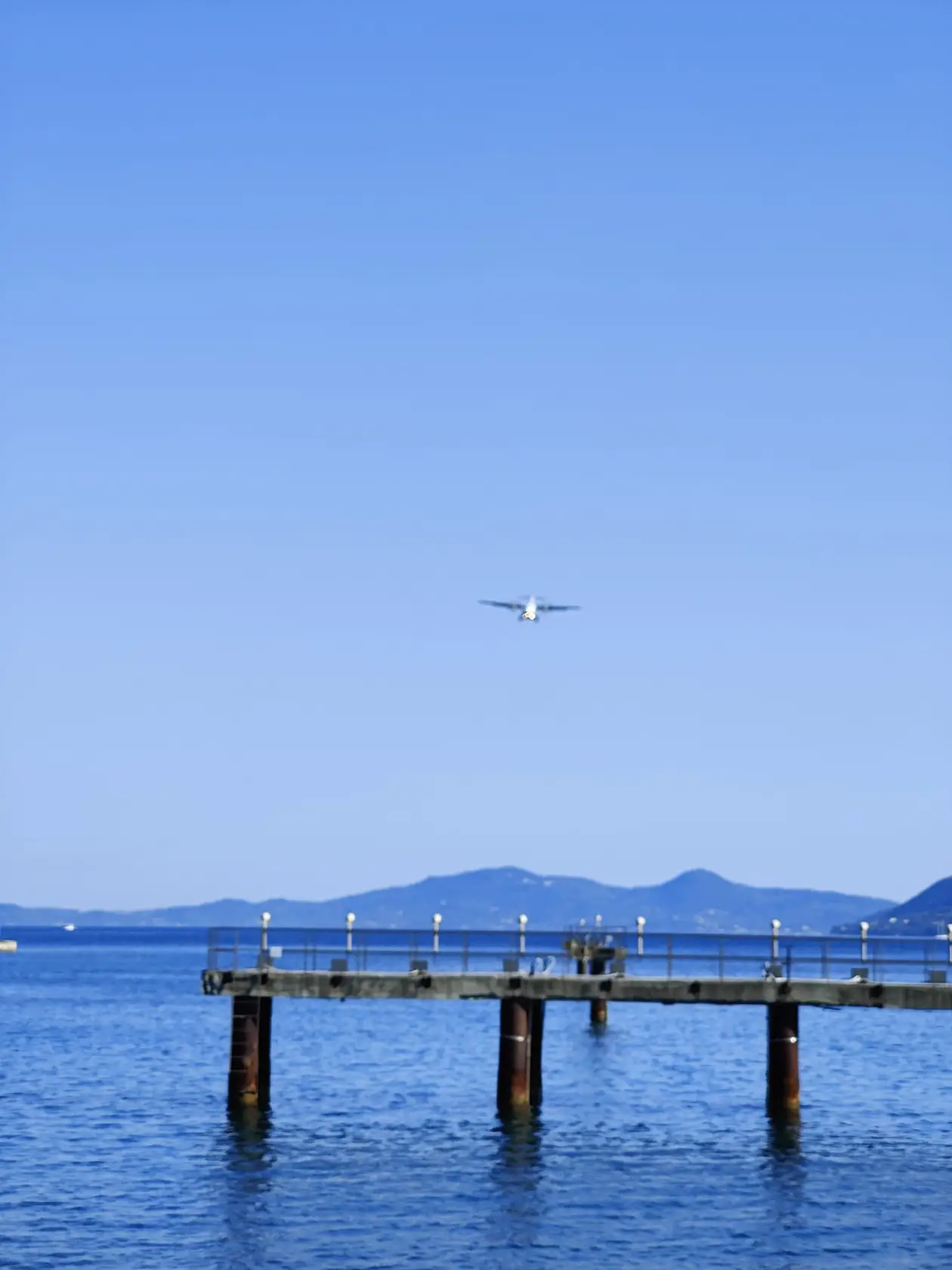 Ein Flugzeug im Anflug am blauen Himmel über einem Steg im Wasser