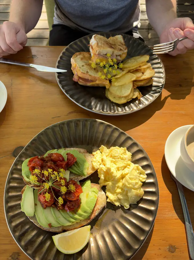 Frühstücksteller mit Avocado, Rührei und Tomaten auf einem Holztisch im Freien