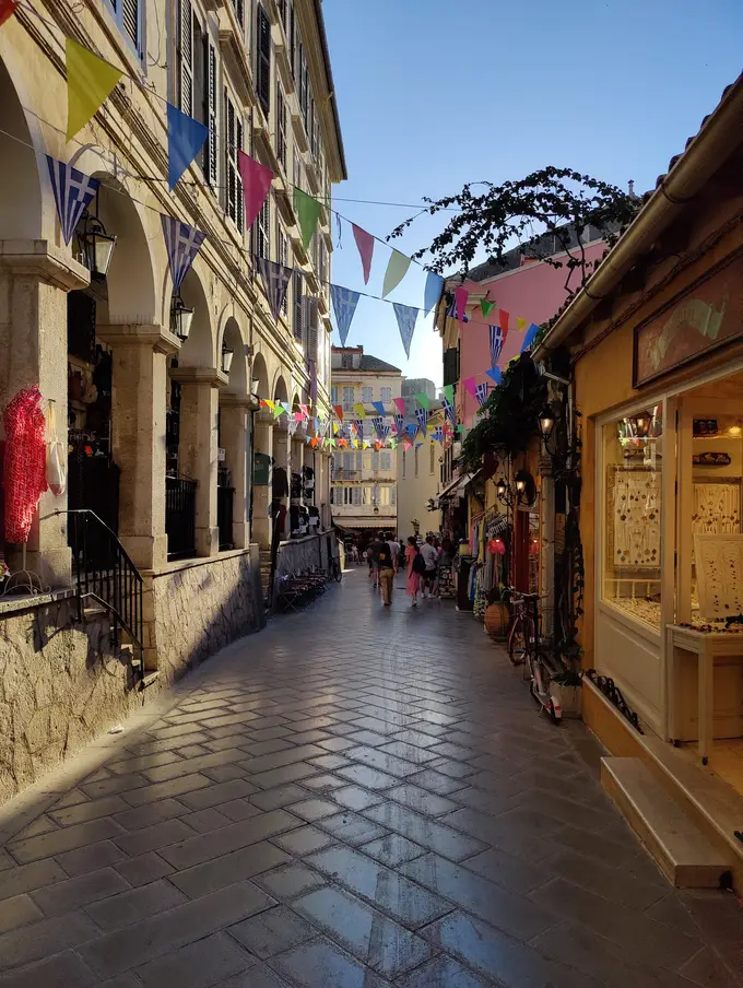 Gasse mit Arkaden auf der linken Seite, glänzendem Pflaster und bunten Wimpeln über der Straße