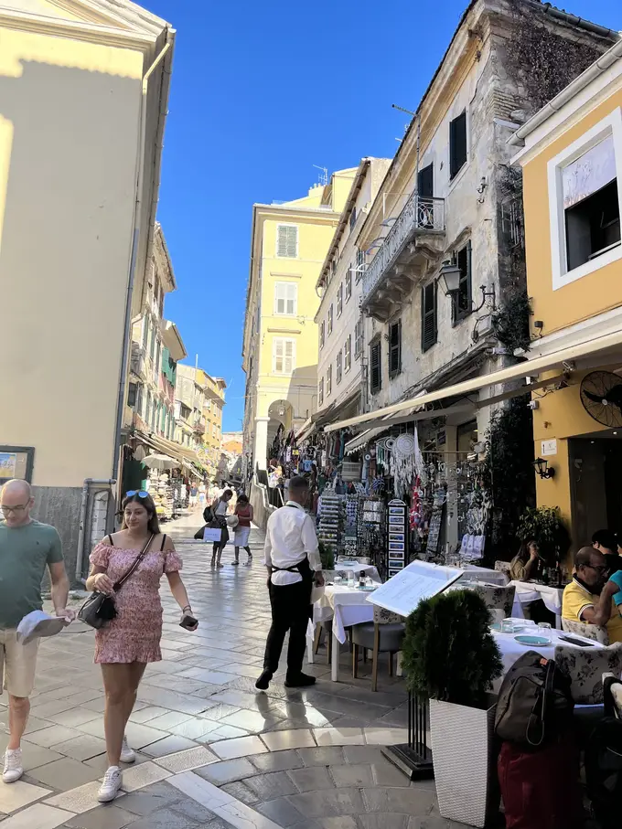 Rebecca in einer Gasse zwischen hohen Häusern, rechts gedeckte Restauranttische