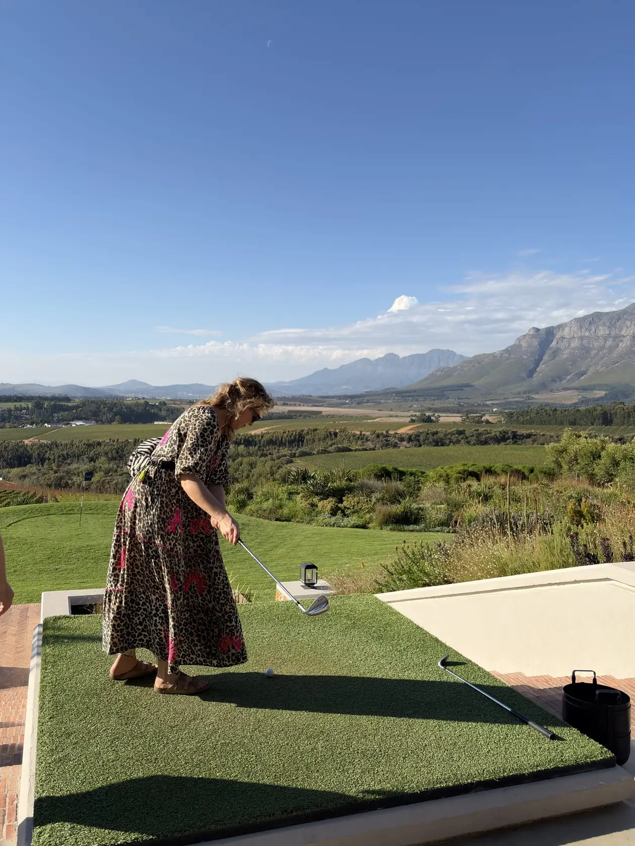 Rebecca beugt sich zum Abschlag auf der Terrasse, im Hintergrund die Weinberge