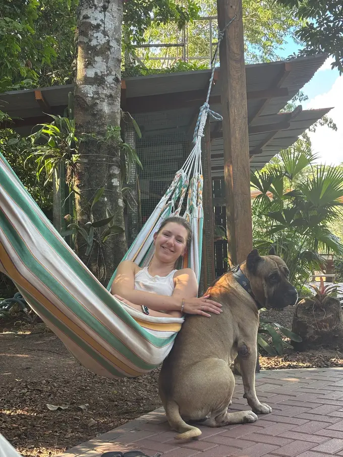 Rebecca liegt lachend in einer gestreiften Hängematte und krault einen großen braunen Hund