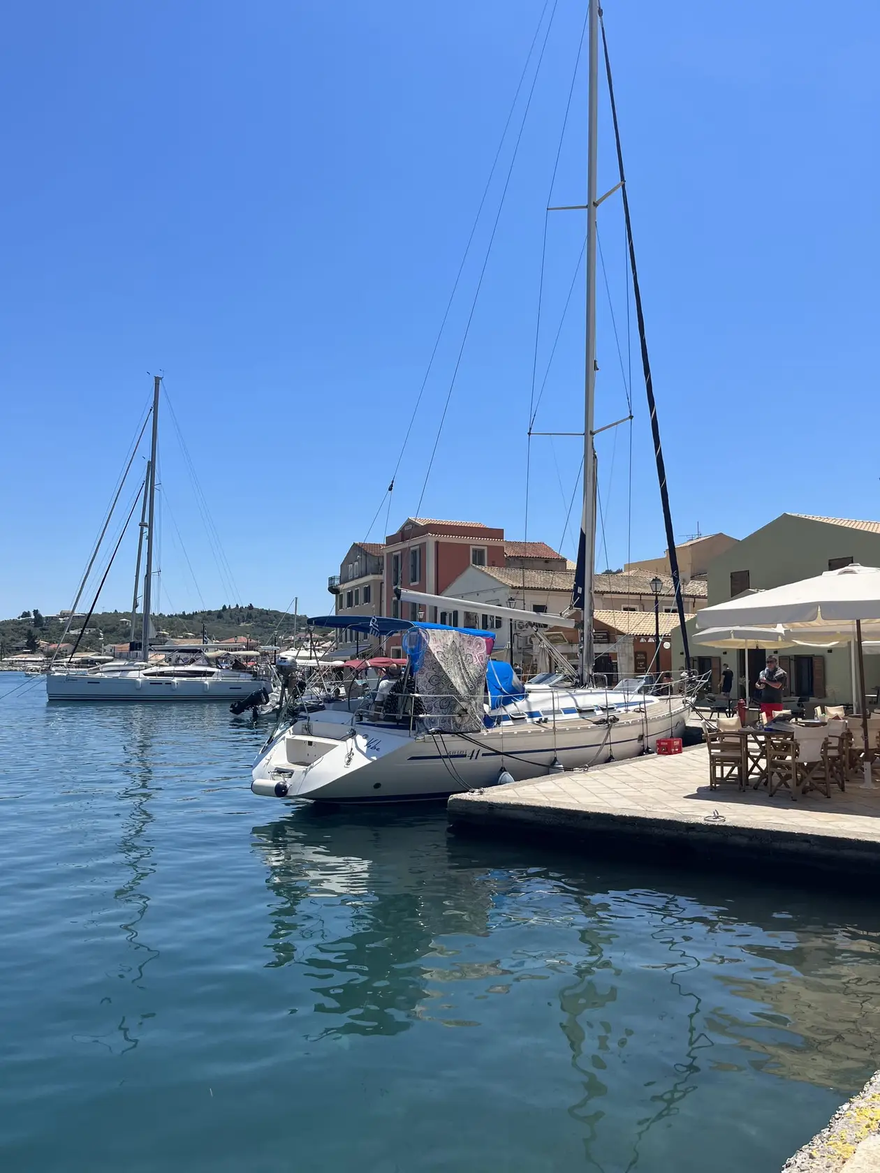 Segelyachten an einem Anleger in Gaios, dahinter Häuser mit Sonnenschirmen am Wasser