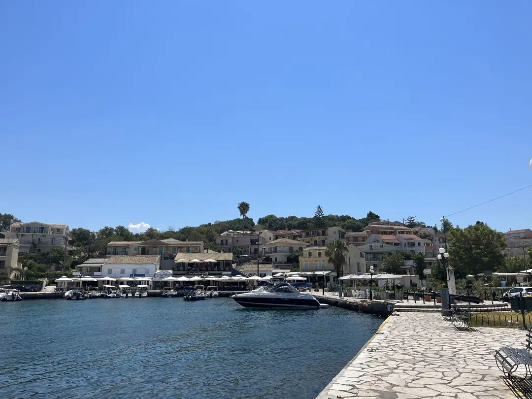 Hafenbecken von Kassiopi mit gepflasterter Mole, einem Motorboot und Häusern am Ufer