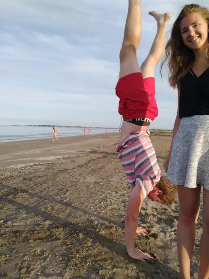 Max macht am Strand einen Handstand, daneben steht Rebecca und lacht